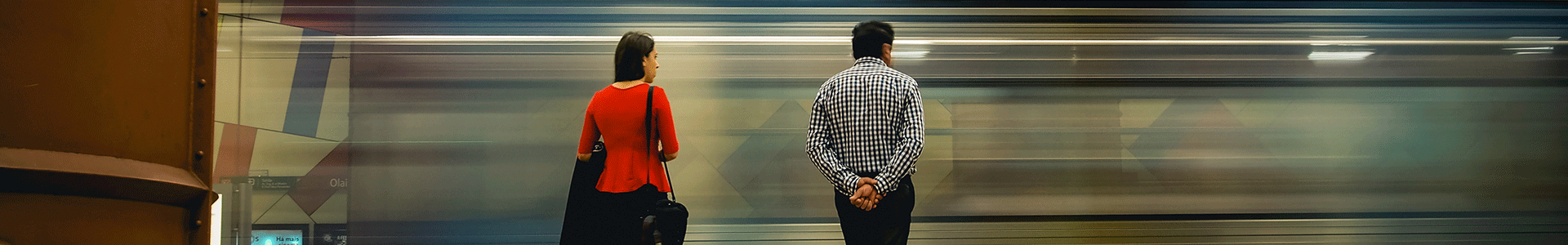 Dois clientes no cais de uma estação de metro observam um comboio a passar.