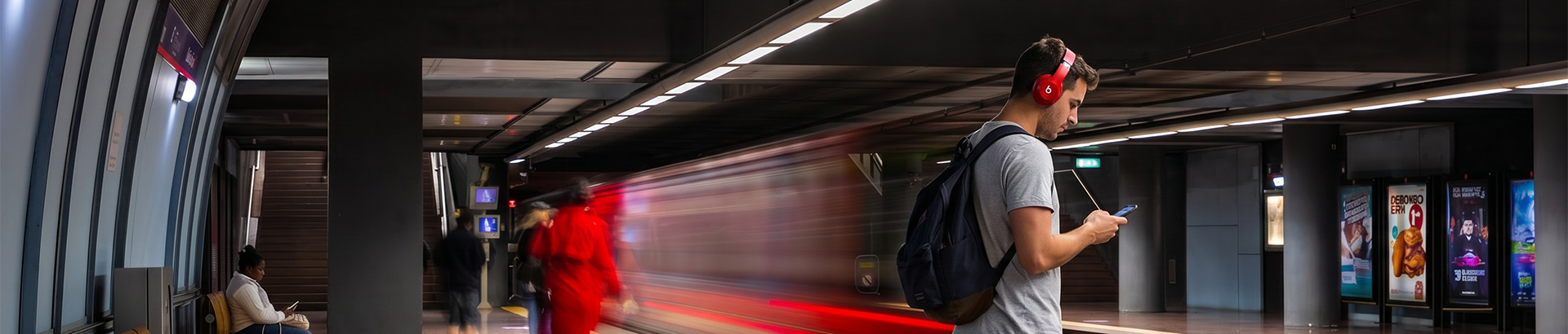 Dois clientes no cais de uma estação de metro observam um comboio a passar.